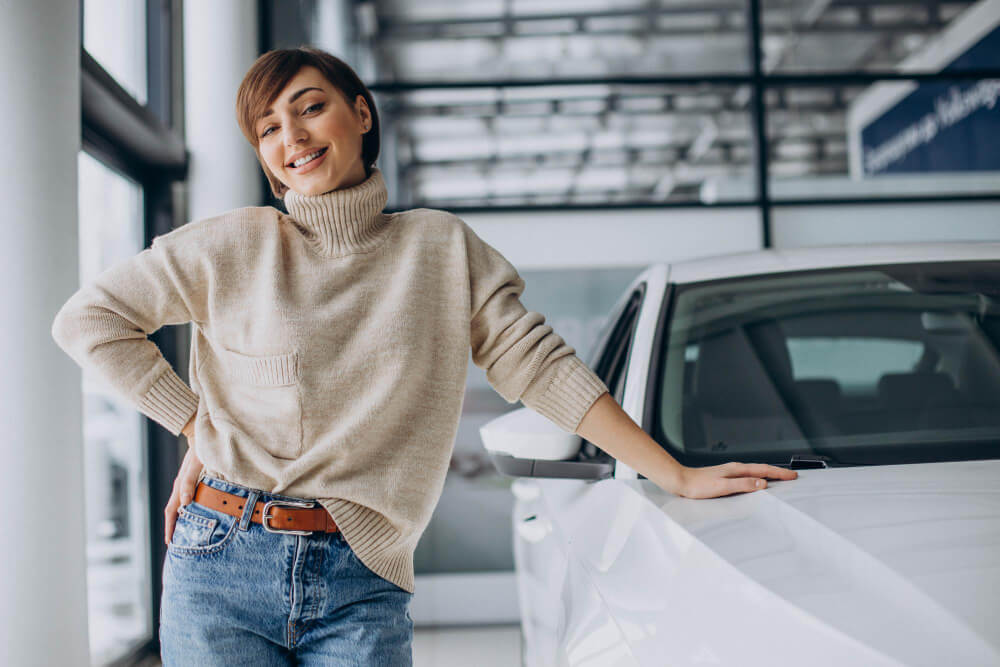 femme qui sourit se tenant appuyée contre une voiture dans un garage automobile